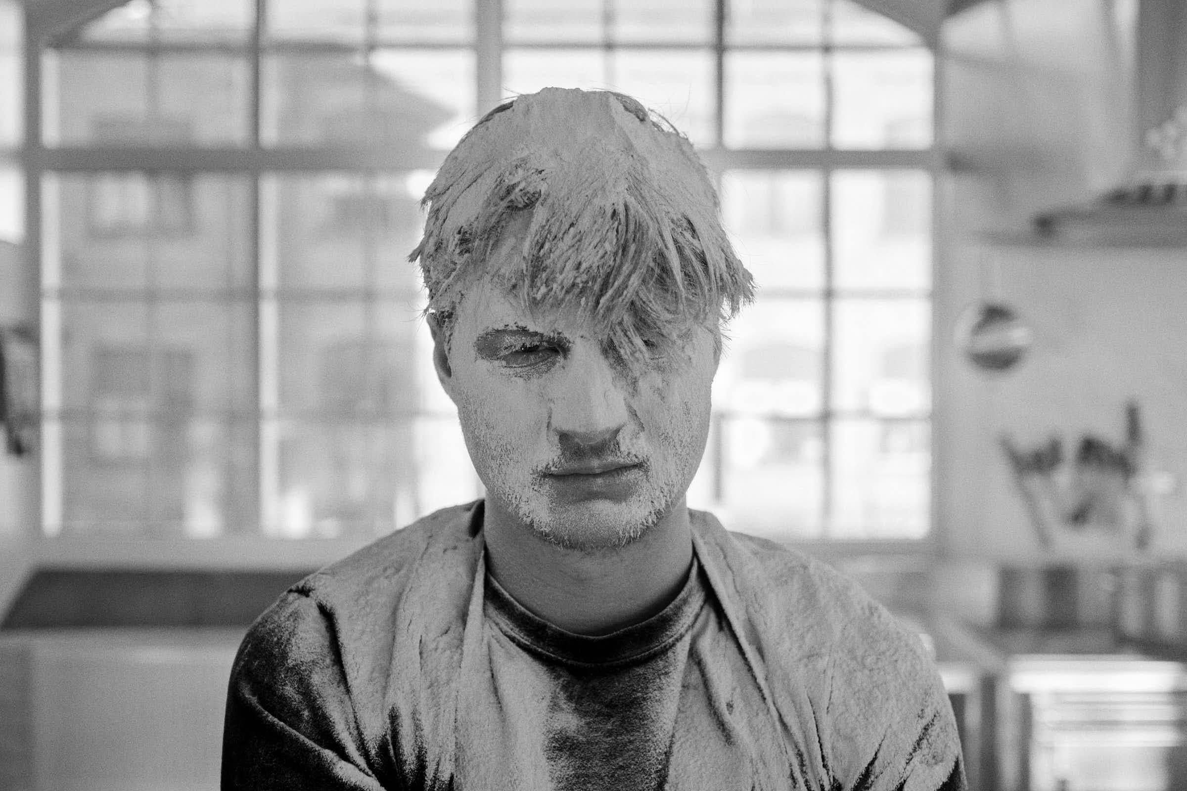 Black and white portrait of Rasmus at Salt Studio Gävle, flour-dusted, industrial windows behind