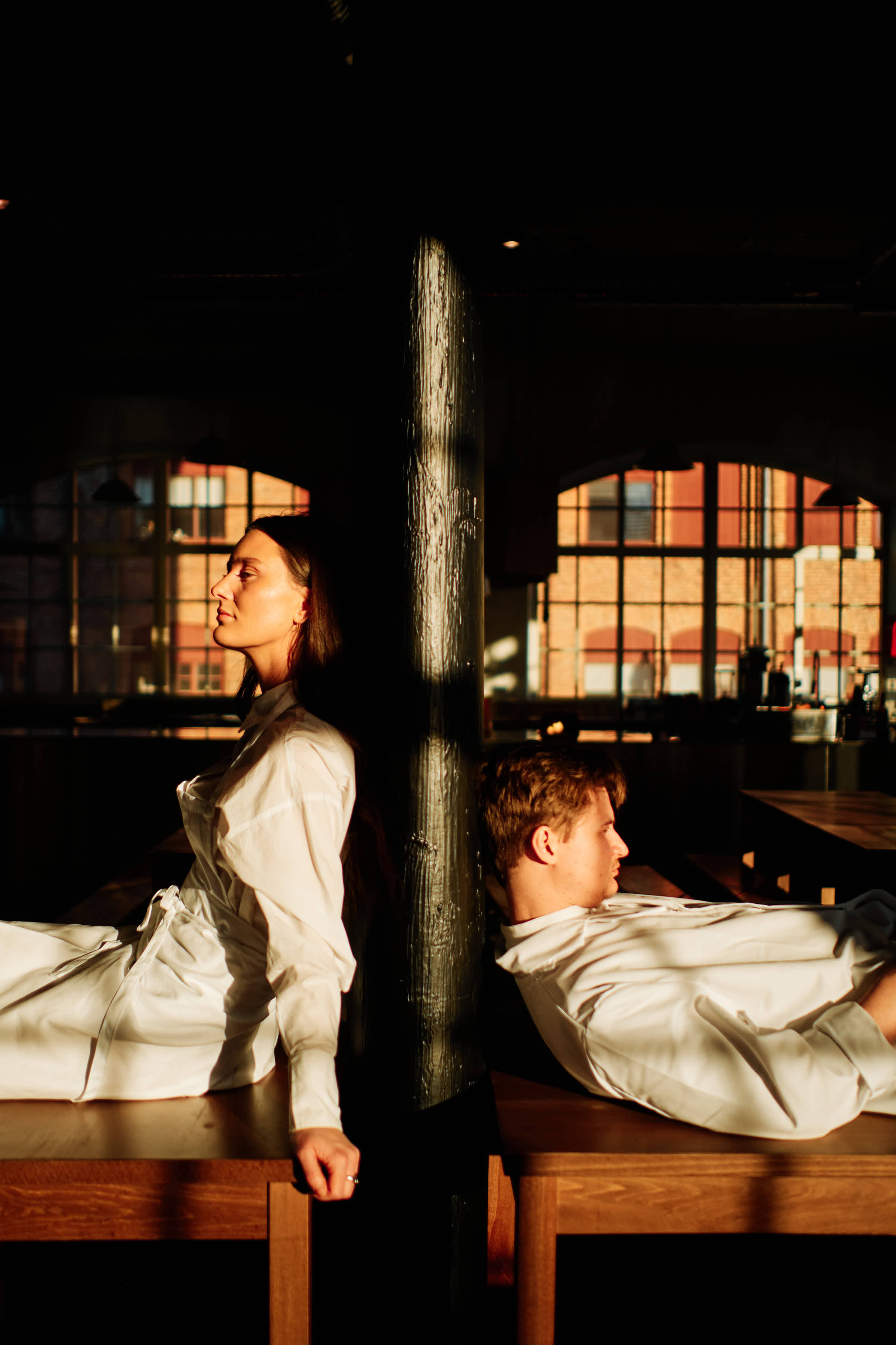 Rasmus and Evelina leaning against wooden post inside Salt Studio Gävle, industrial windows behind